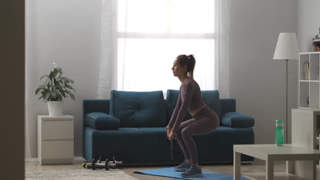 sporty-woman-dressed-sportswear-is-doing-squats-with-weight-in-hands-training-body-keeping-fit-home-fitness-exercises-full-length-shot-in-apartment